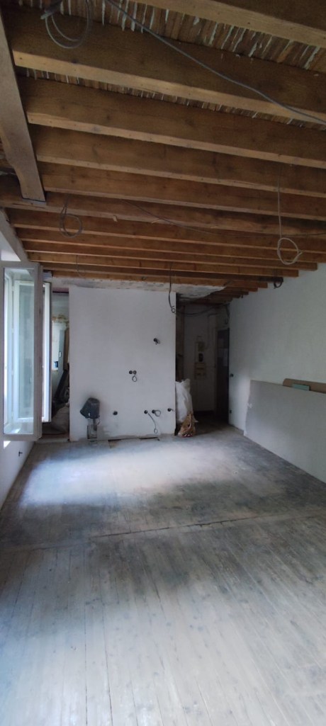Pièce avant rénovation avec parquet brut, poutres apparentes et mur nu